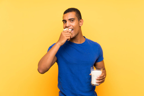Giovane bello bruna uomo su sfondo giallo avendo latte per la prima colazione e tenendo torta muffin
 - Foto, immagini