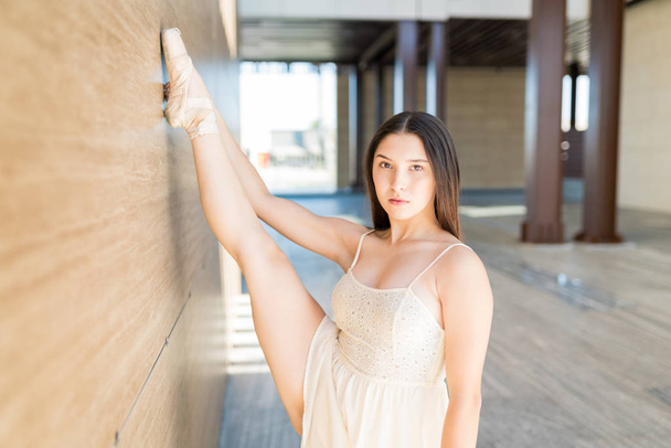 Dans provaları sırasında kendine güvenen esnek balerin bacağını duvara uzatıyor. - Fotoğraf, Görsel