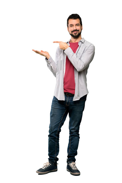 Celovečerní snímek pohledný muž s plnovousem drží imaginární copyspace na dlani vložit inzerát izolované bílém pozadí - Fotografie, Obrázek