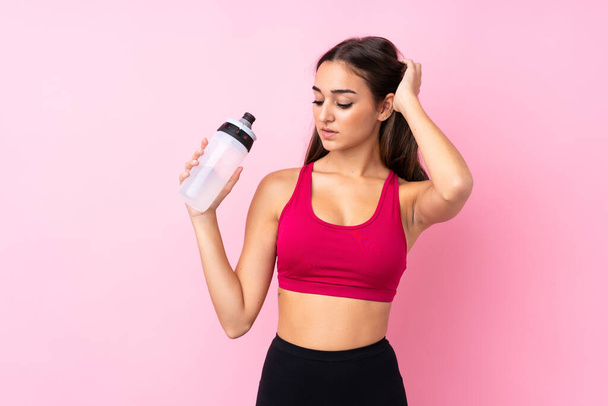 Giovane ragazza sportiva su sfondo rosa isolato con bottiglia d'acqua sportiva - Foto, immagini