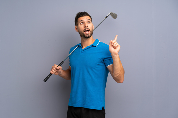 Όμορφος νεαρός που παίζει γκολφ με σκοπό να συνειδητοποιήσει τη λύση σηκώνοντας το δάχτυλό του. - Φωτογραφία, εικόνα