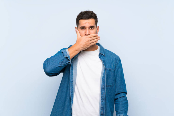 Handsome man over isolated blue background covering mouth with hands - Photo, Image