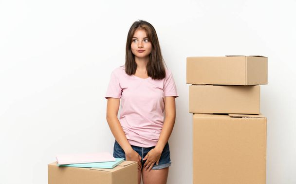 Молодая девушка переезжает в новый дом среди коробок стоя и глядя в сторону
 - Фото, изображение