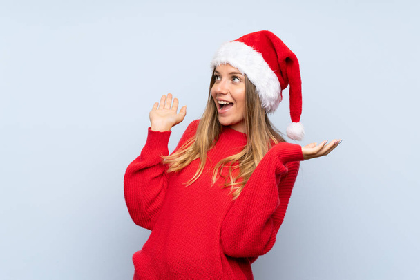 Chica con sombrero de Navidad sobre fondo azul aislado con expresión facial sorpresa
 - Foto, Imagen