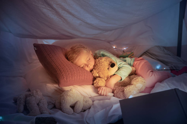 Little girl lying in a teepee, sleeping with the flashlight - Photo, image