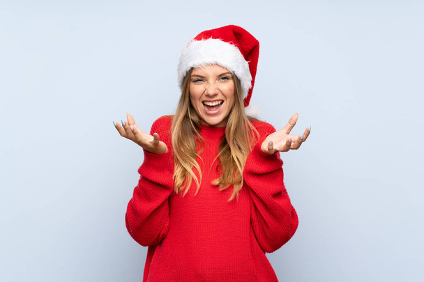 Chica con sombrero de Navidad sobre fondo azul aislado infeliz y frustrado con algo
 - Foto, Imagen