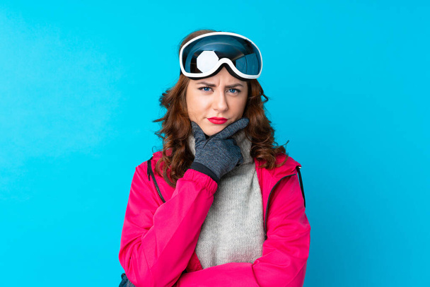 Лыжная женщина в сноубордистских очках над изолированной голубой стеной думает об идее
 - Фото, изображение