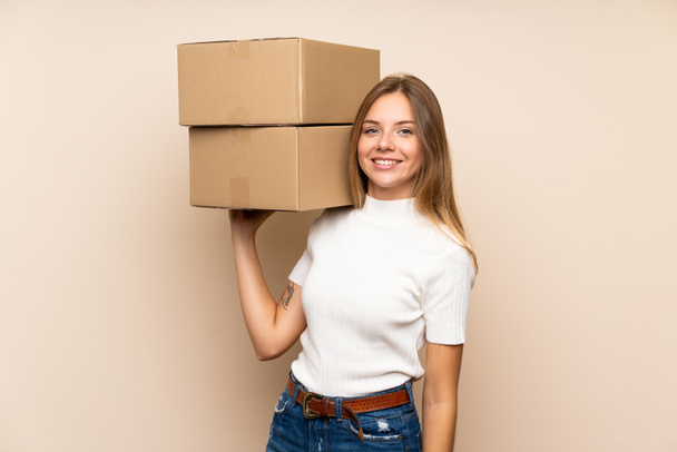 Young blonde woman over isolated background holding a box to move it to another site - Фото, зображення