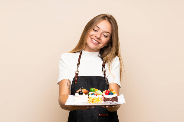 Young blonde woman over isolated background holding mini cakes - Photo, image