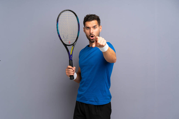 Bonito jovem jogador de tênis homem surpreso e apontando frente
 - Foto, Imagem