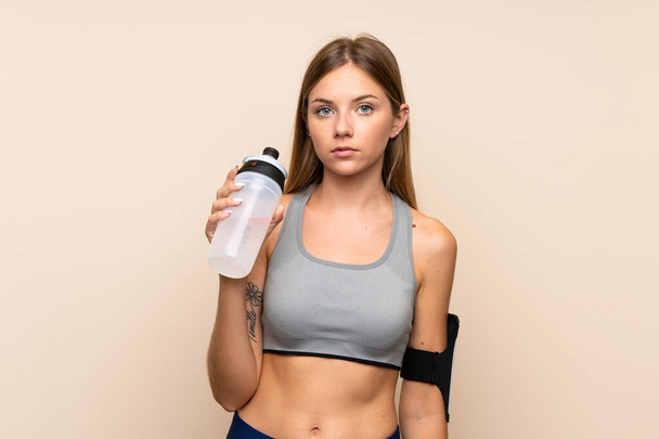 Young blonde sport girl over isolated background with sports water bottle - Фото, изображение