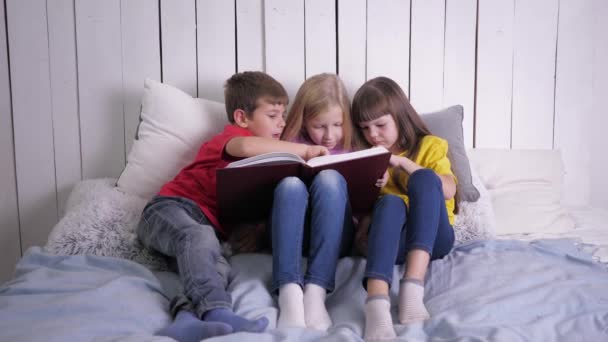 edukacja, inteligentne dzieci w wielobarwnych ubraniach uczą się czytać w domu siedząc na kanapie - Materiał filmowy, wideo