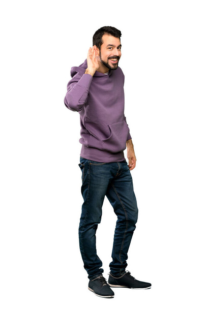Full-length shot of Handsome man with sweatshirt listening to something by putting hand on the ear over isolated white background - Photo, image