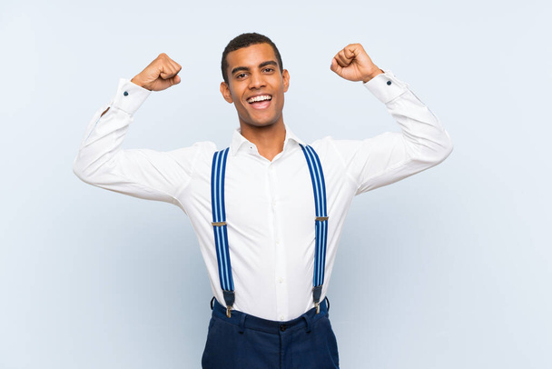 Young handsome brunette man with suspenders over isolated background celebrating a victory - Φωτογραφία, εικόνα