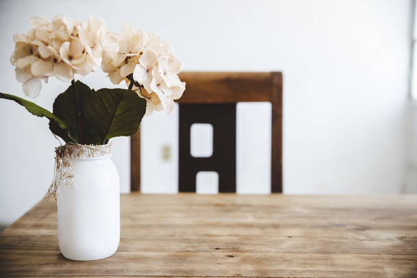 Closeup shot of white flowers in a white jar on a wooden table with a blurred background - Φωτογραφία, εικόνα