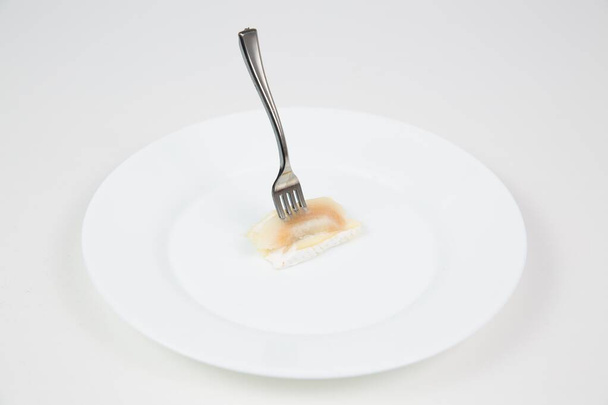 Closeup shot of a fork stuck in a piece of fish in a white plate isolated on a white background - Fotoğraf, Görsel