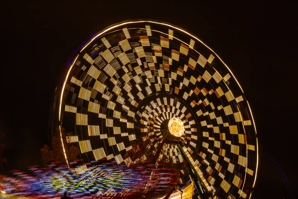 Two rides in motion in amusement park, night illumination. Long exposure. - Photo, Image