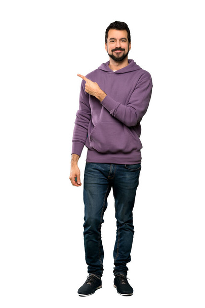 Full-length záběr pohledný muž s mikinou ukazuje do strany prezentovat produkt přes izolované bílé pozadí - Fotografie, Obrázek