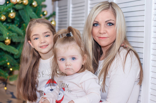 Μαμά και κόρες στο χριστουγεννιάτικο δέντρο. Χριστούγεννα. Αδερφές. Καλά Χριστούγεννα και καλές γιορτές. Χαρούμενη μαμά και οι χαριτωμένες κόρες της ανταλλάσσουν δώρα.. - Φωτογραφία, εικόνα