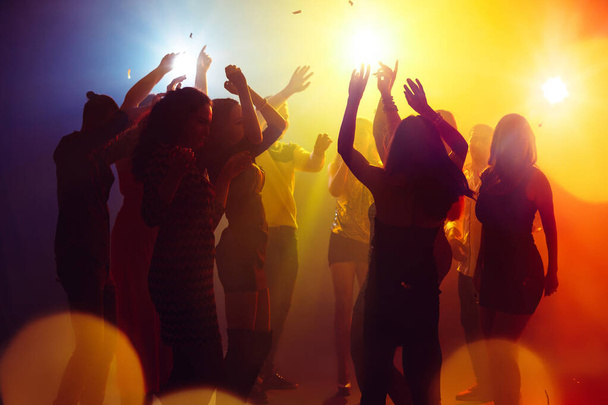 シルエットの人々の群衆はパーティーの背景にカラフルなネオンに対して手を上げます - 写真・画像