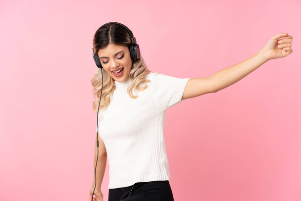Chica adolescente sobre fondo rosa aislado usando el móvil con auriculares y bailando
 - Foto, imagen