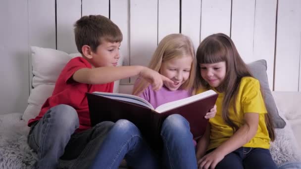 niños inteligentes en ropa multicolor leer libro mientras están sentados en la cama en casa durante las vacaciones
 - Metraje, vídeo