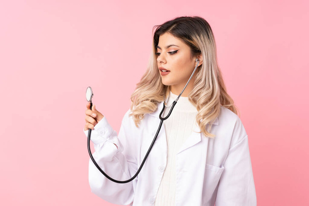 Teenager girl over isolated pink background with doctor gown - Fotografie, Obrázek