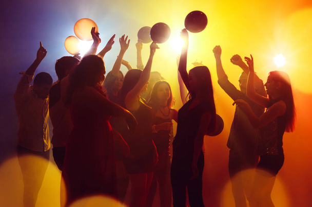 A crowd of people in silhouette raises their hands against colorful neon light on party background - Фото, зображення