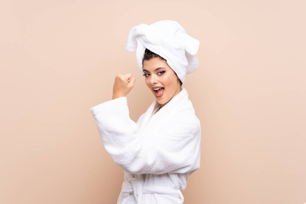 Teenager girl in a bathrobe over isolated background making strong gesture - Фото, изображение