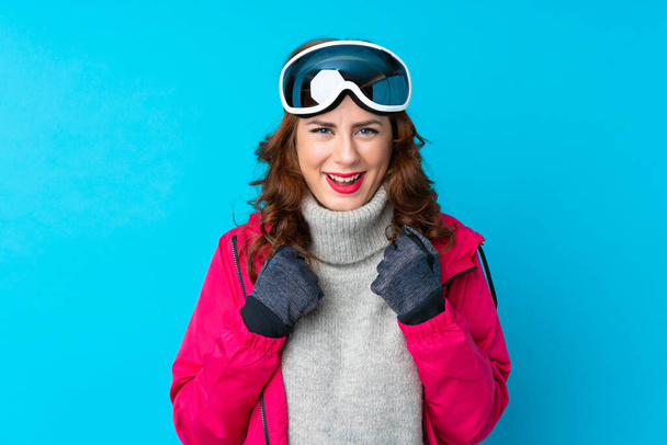 Kar kayağı gözlüklü kayakçı kadın mavi duvarın üstünde zaferi kutluyor. - Fotoğraf, Görsel