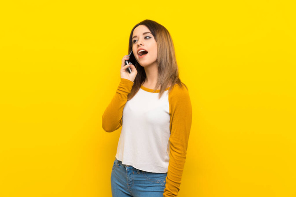 Mulher bonita sobre a parede amarela isolada mantendo uma conversa com o telefone móvel
 - Foto, Imagem
