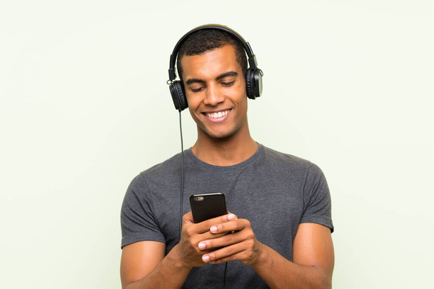 Jonge knappe man luisteren muziek met een mobiele over geïsoleerde groene muur - Foto, afbeelding