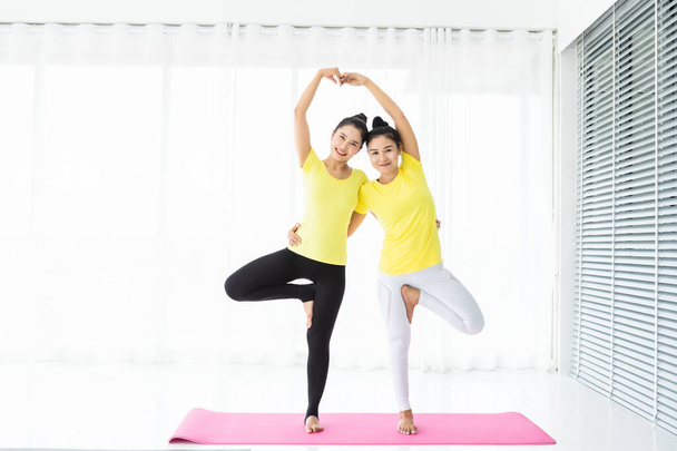 Two young Asian women workout practicing yoga in yellow dress or - Fotó, kép