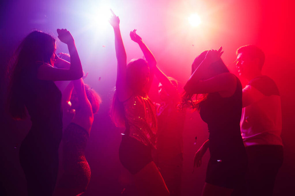 Silüetli bir kalabalık parti arka planındaki renkli neon ışığa karşı ellerini kaldırıyor. - Fotoğraf, Görsel