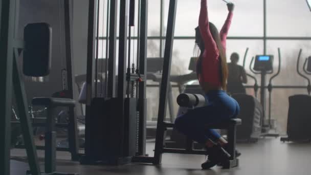 Krafttraining am Morgen im Fitnessstudio. Beim Training in einem Raum mit großen Fenstern im Hintergrund benutzt eine Frau einen Ellipsoid und ein Laufband - Filmmaterial, Video