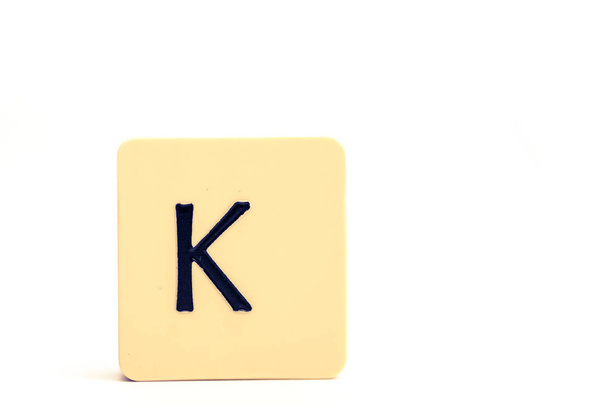 Dark letter K on a pale yellow square block isolated on white ba - Photo, Image