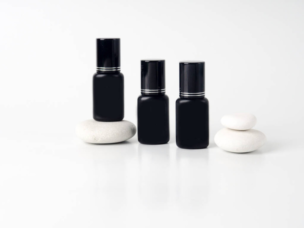 three black cosmetic jars on stones. Set of cosmetic products on a white background. Cosmetic package collection for cream, soups, foams, shampoo.Natural beauty blank label for branding mock-up concep - Valokuva, kuva