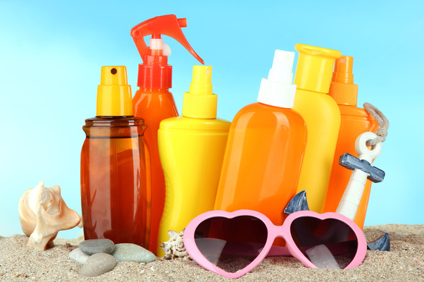 Bottles with suntan cream and sunglasses, on blue background - Photo, image