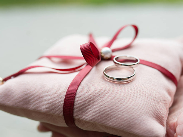 ślubne białe złote obrączki na różowej poduszce jako symbole miłości i małżeństwa - Zdjęcie, obraz