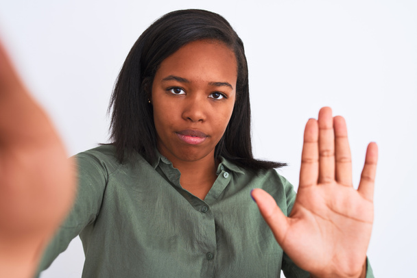 Kaunis nuori afrikkalainen amerikkalainen nainen ottaa selfie yli eristetty tausta avoimella kädellä tekee stop merkki vakava ja luottavainen ilme, puolustus ele
 - Valokuva, kuva