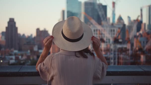 Młoda dziewczyna w kapeluszu patrzy z drapacza chmur - Materiał filmowy, wideo
