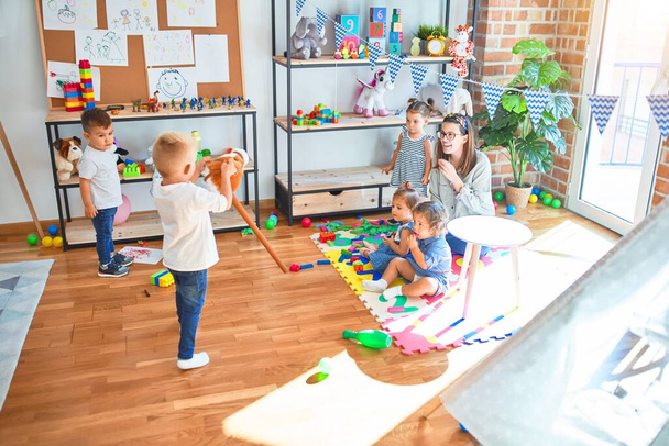 Belo professor e grupo de crianças brincando em torno de lotes de brinquedos no jardim de infância
 - Foto, Imagem