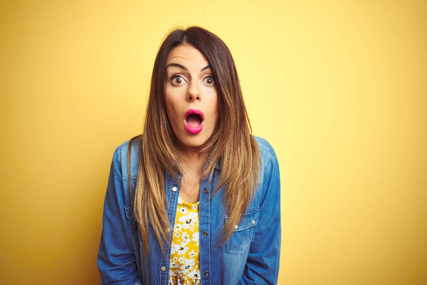 Young beautiful woman standing over yellow isolated background afraid and shocked with surprise and amazed expression, fear and excited face. - Photo, Image