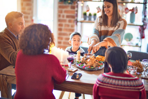 Beautiful family smiling happy and confident. One of them curving roasted turkey celebrating christmas at home - Photo, Image