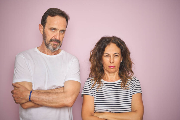 Beautiful middle age couple together standing over isolated pink background skeptic and nervous, disapproving expression on face with crossed arms. Negative person. - 写真・画像