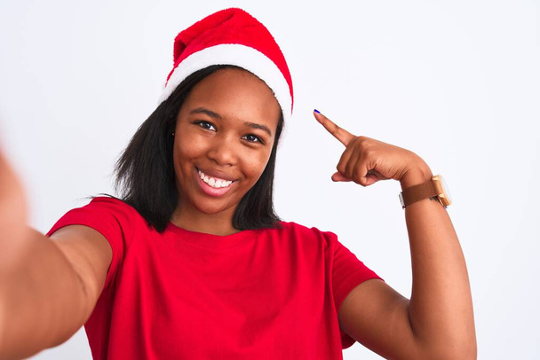 Giovane donna afroamericana indossando cappello di Natale e prendendo un selfie su sfondo isolato molto felice indicando con mano e dito
 - Foto, immagini