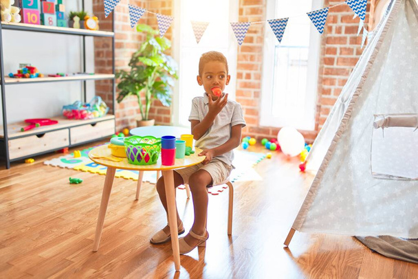 Hermoso niño afroamericano jugando con comida plástica y juguete de cubiertos en el jardín de infantes
 - Foto, Imagen