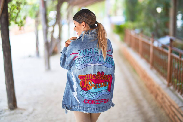 Young beautiful woman wearing denim jacket standing backwards at the town park - Photo, Image