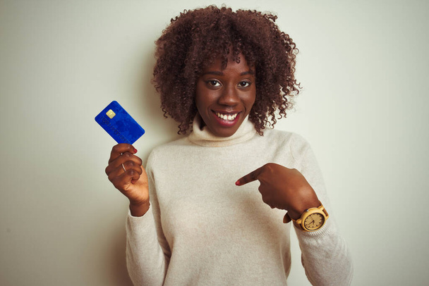 Молодая африканская афро-женщина держит кредитку стоя на изолированном белом фоне с удивленным лицом указывая пальцем на себя
 - Фото, изображение