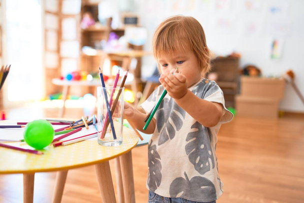 Adorable niño sosteniendo lápices alrededor de un montón de juguetes en el jardín de infantes
 - Foto, Imagen
